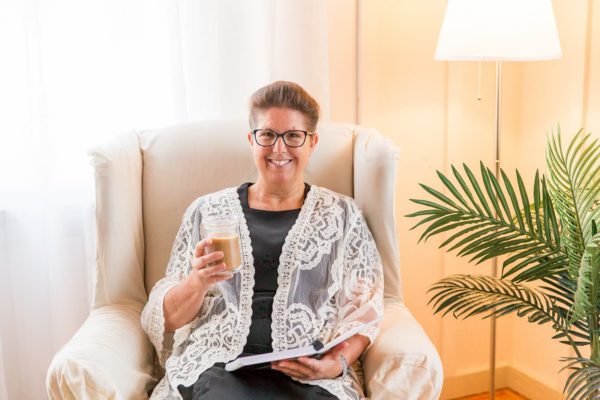 Smiling Woman with Open Planner and Coffee Sitting in Chair